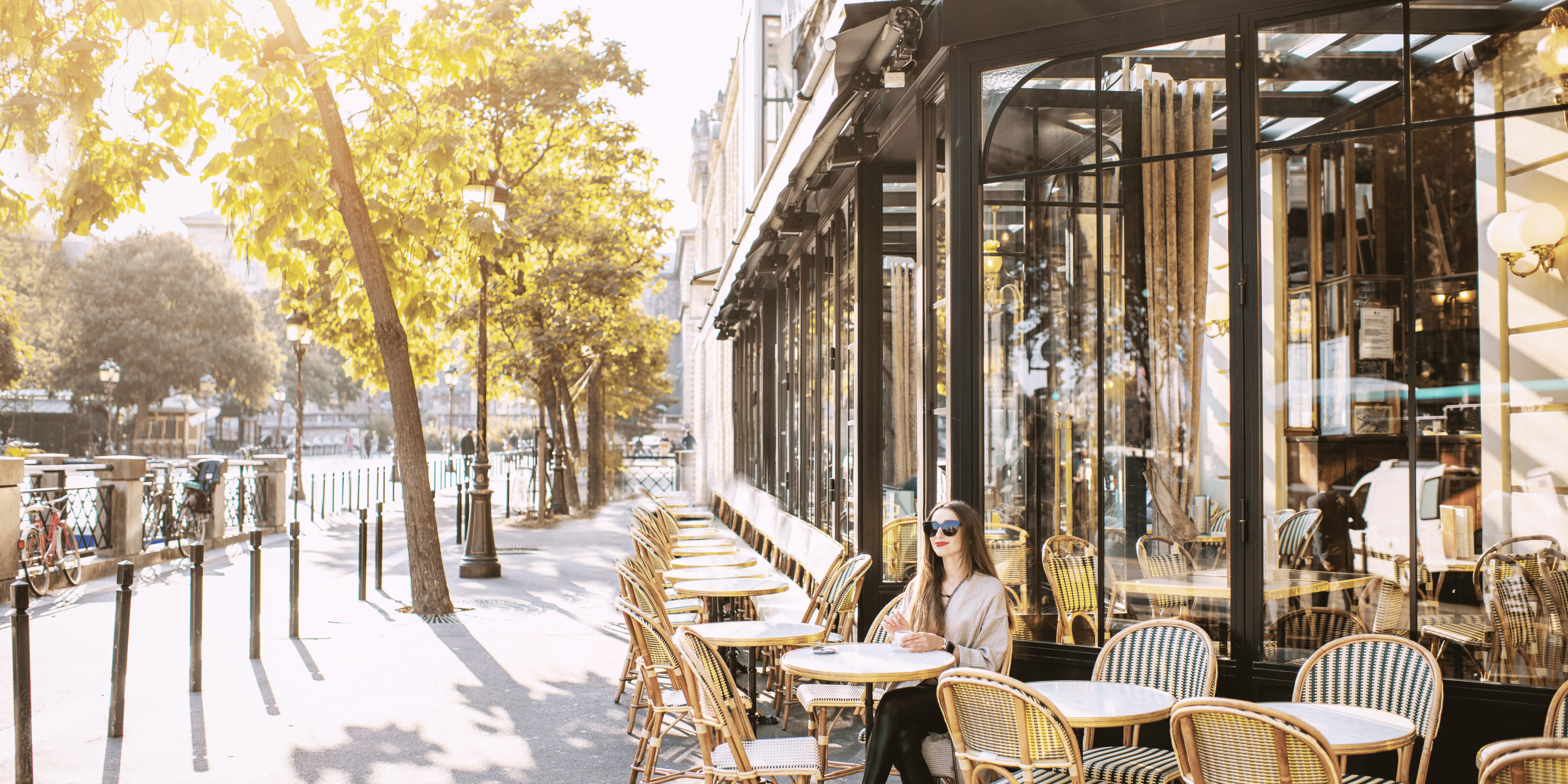 Woman Dining at French Street Corner Café Woman sitting at an outdoor French restaurant terrace surrounded by trees and street views