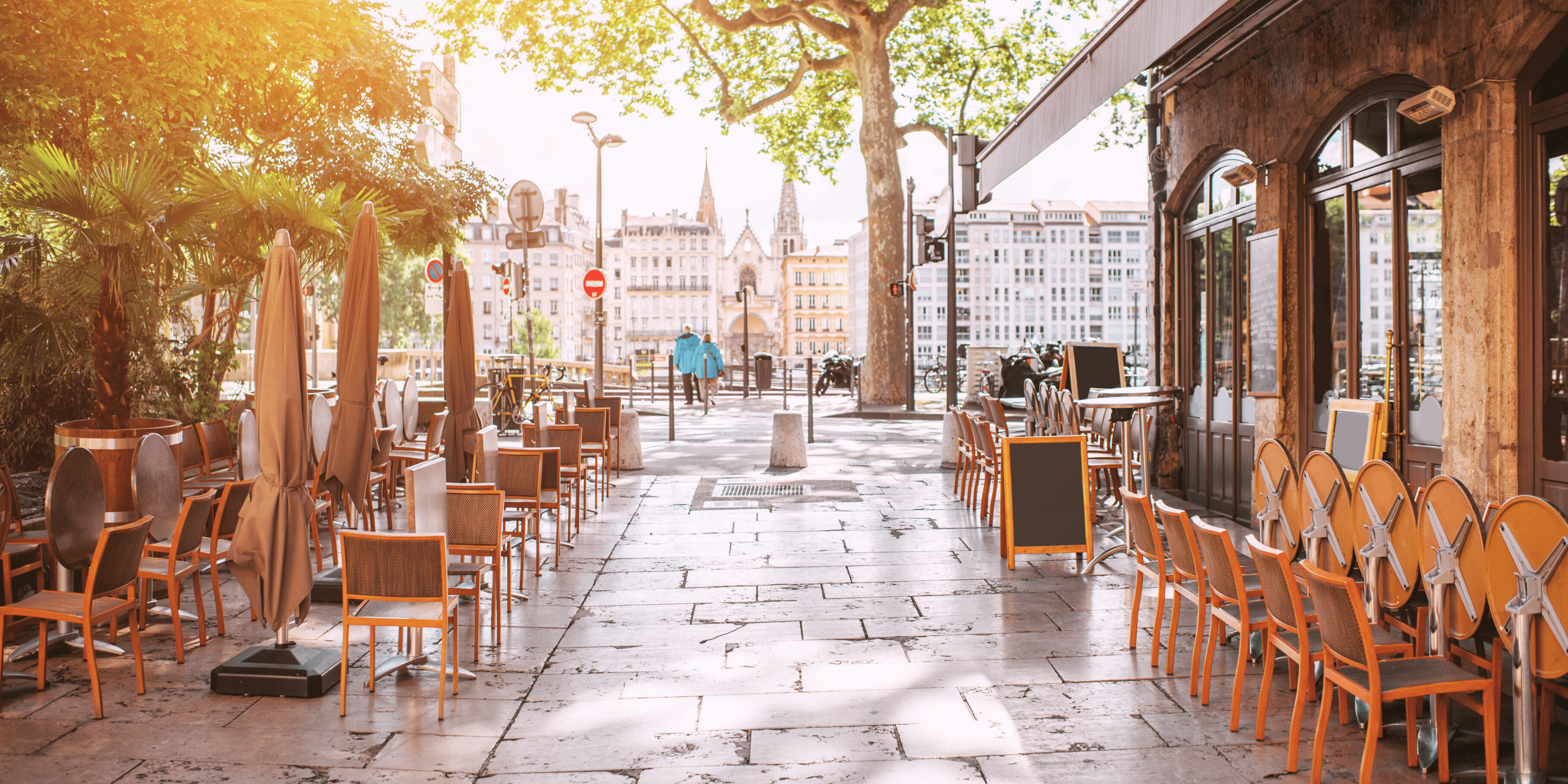 French Café Terrace Setup in the Morning French restaurant preparing outdoor terrace seating on a quiet street lined with trees and traditional buildings