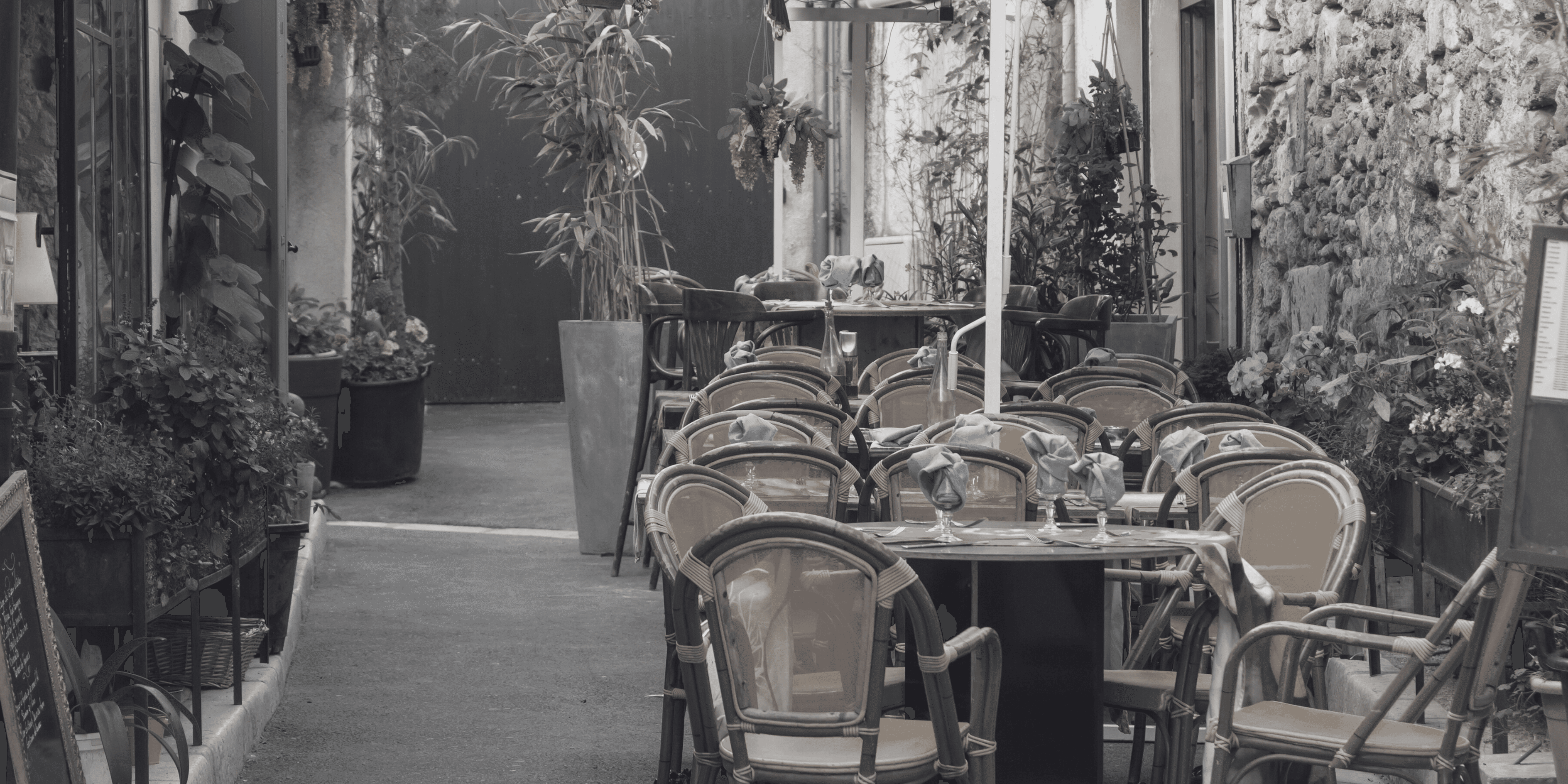 French Outdoor Café Seating – Black & White Black and white image of French café tables and plants outside a restaurant